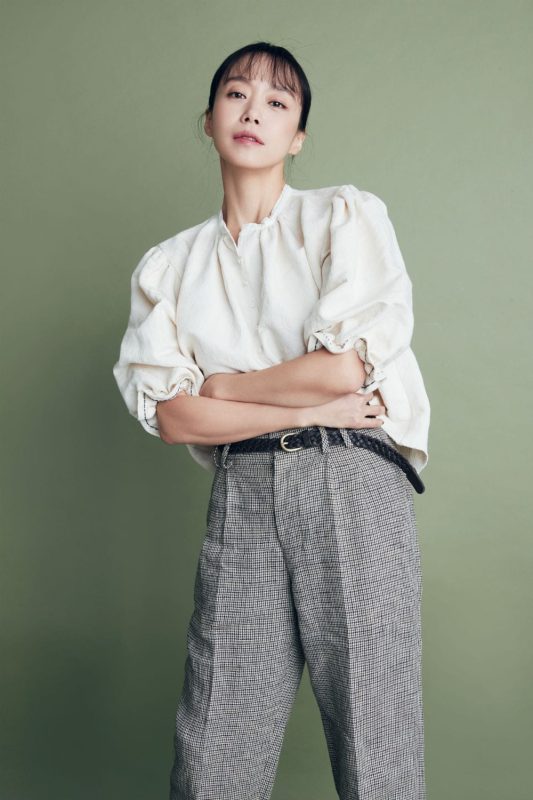 Jeon Do-Yeon stood with her arms crossed in front of a green backdrop. 