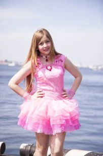 sakura posing in front of the ocean with both hands on her hips. she is wearing a fluffy, short pink dress.